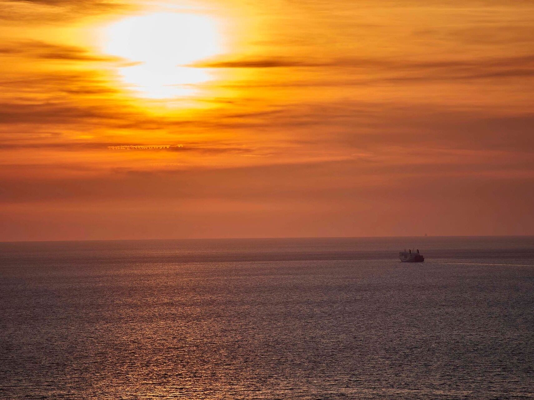 Atardecer sobre un mar tranquilo con un barco a lo lejos.