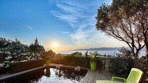 Een houten terras met een zwembad, een groene stoel en uitzicht op de ondergaande zon boven het water.