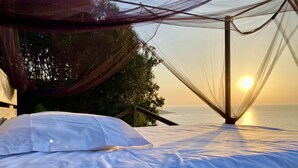 A bed with white linens, a canopy, and a view of the sea at sunset. - Double room-Deluxe-Ensuite with Shower-Sea view (Belvédère-Campomoro)