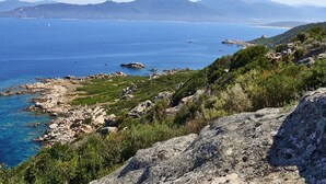 A coastal landscape with rocky terrain, greenery, and a clear view of the sea and distant mountains. - Double room-Deluxe-Ensuite with Shower-Sea view (Belvédère-Campomoro)