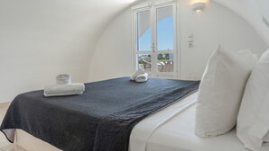 Un dormitorio con techo curvo, cama con sábanas blancas, colcha oscura y ventana con vistas.