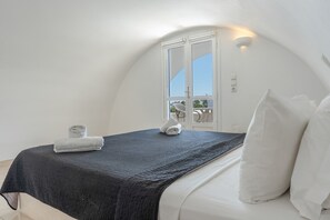 Un dormitorio con techo curvo, cama con sábanas blancas, colcha oscura y ventana con vistas.