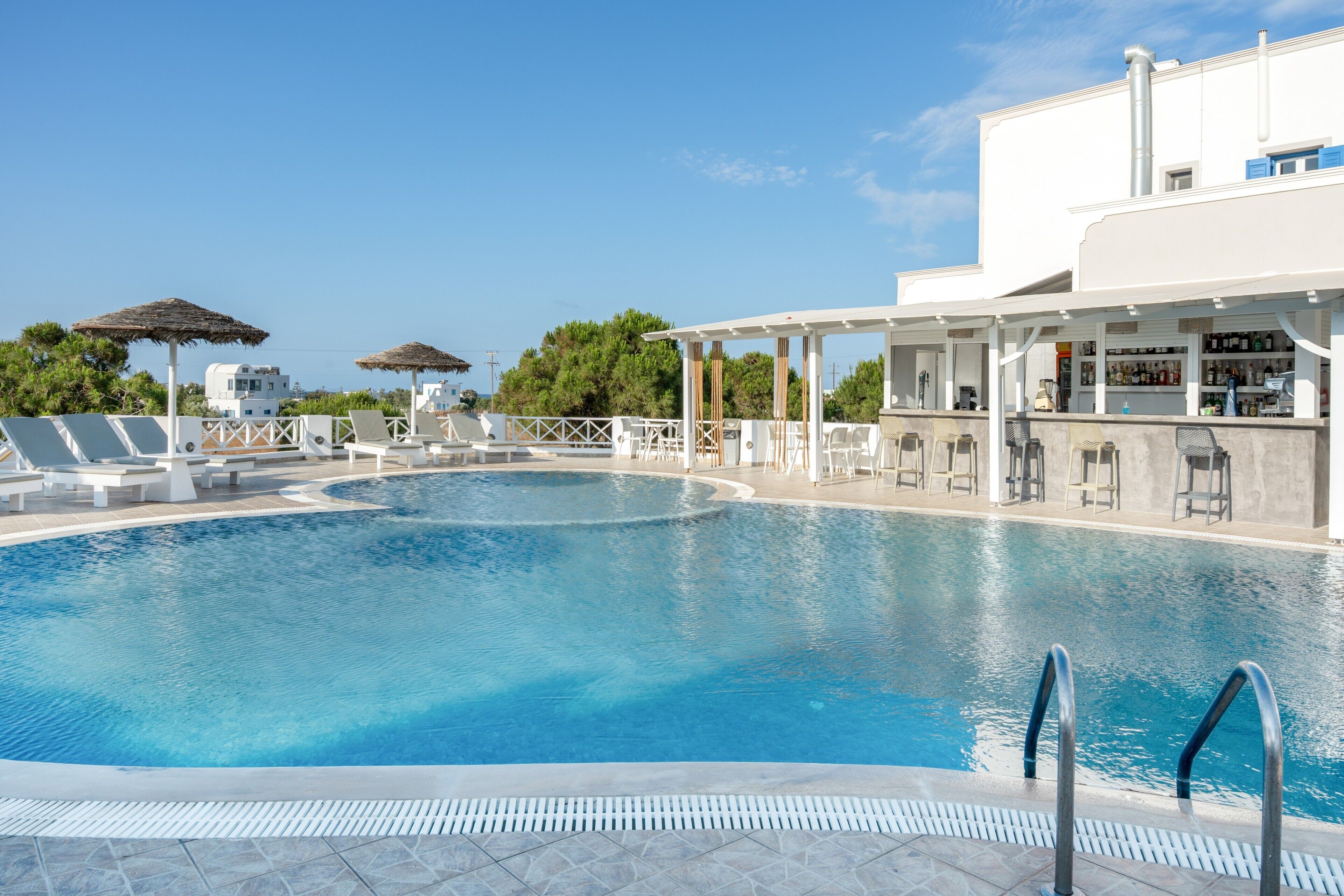 A swimming pool with lounge chairs and umbrellas, a bar area, and a building with a white facade.