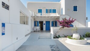 Un edificio blanco con contraventanas azules, una zona de recepción y una escalera que lleva a la entrada.