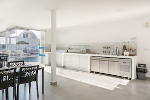 Cocina moderna con separador de vidrio, armarios blancos y vista a una zona de piscina.