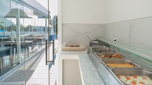 Un espace buffet proposant différents plats, une cloison en verre et une vue sur l’extérieur.