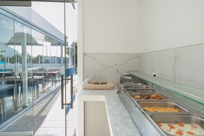 Un espace buffet proposant différents plats, une cloison en verre et une vue sur l’extérieur.