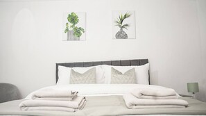 A neatly made bed with pillows and a folded blanket, a bedside lamp, and two framed plant illustrations on the wall. - Sleeps 4, Great for Groups, Free Parking Kent (Gillingham)