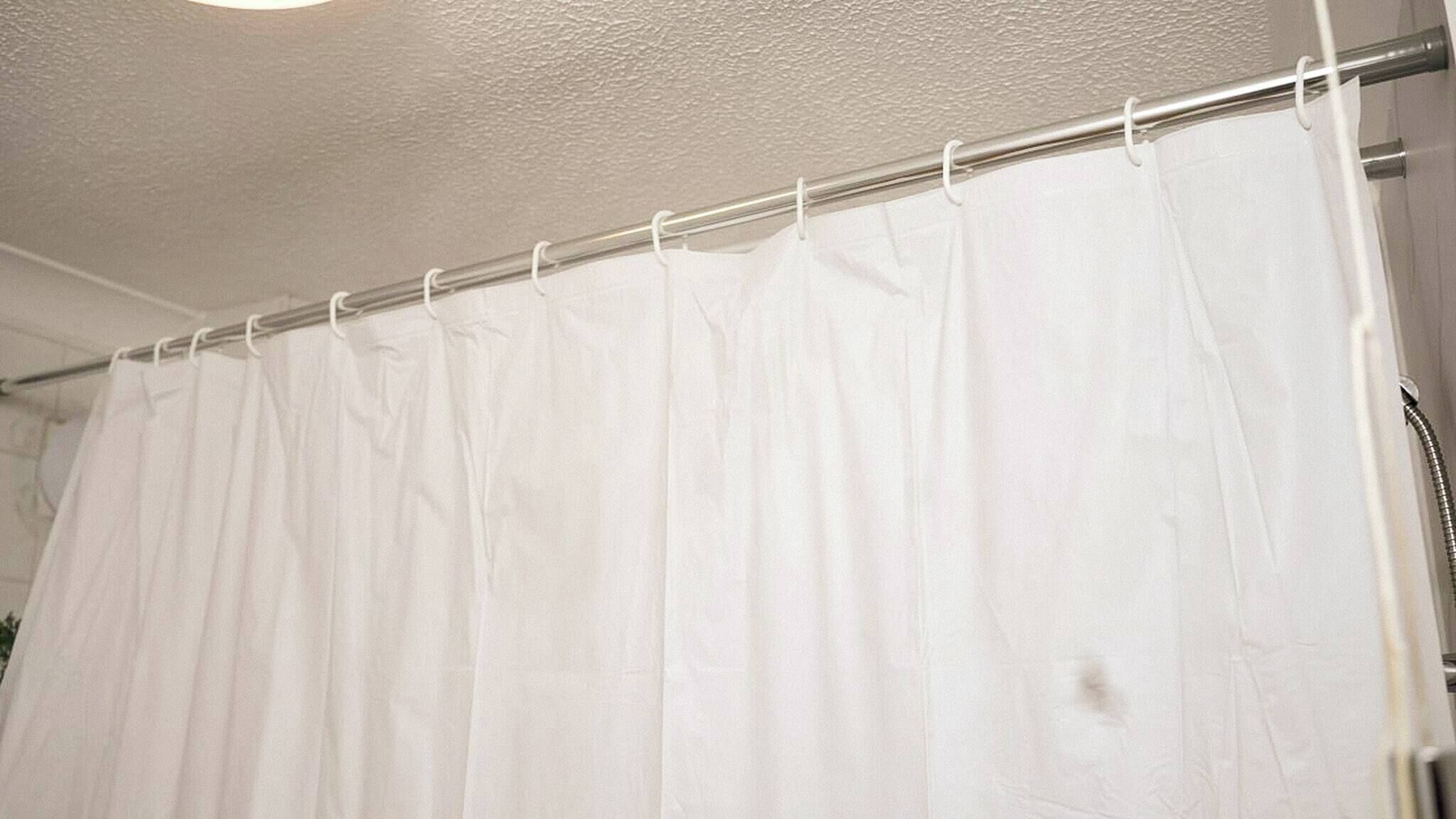 A white shower curtain with a metal rod.