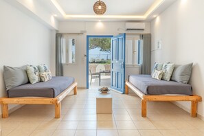 Ein Zimmer mit zwei Betten, einem kleinen Tisch und einer Tür, die nach draußen führt.