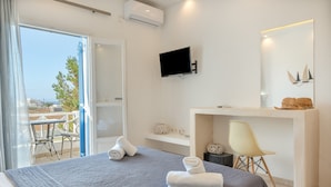 Een moderne hotelkamer met een bed, een bureau, een televisie en een balkon met buitenmeubilair.