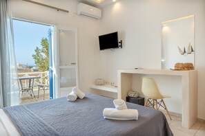 Une chambre d’hôtel moderne équipée d’un lit, d’un bureau, d’une télévision et d’un balcon avec mobilier d’extérieur.