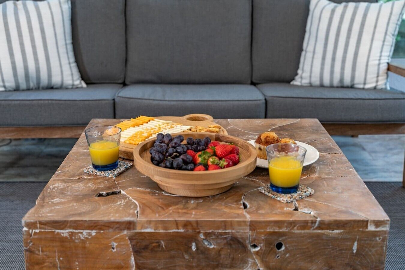 Ein Frühstück auf einem Holztisch mit einer Obstschale, einem Gebäckteller und Gläsern Orangensaft.