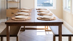 A dining table with placemats, a bench, and a view of the outside through a window. - Circle View Cottage|Hot Tub·Shed Bar·Walk to Beach (Atlantic Beach)