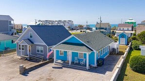 A two-story building with a blue exterior and a grey roof, featuring a small porch with two chairs and a flag. - Circle View Cottage|Hot Tub·Shed Bar·Walk to Beach (Atlantic Beach)