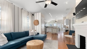 A modern living room with a blue sofa, a woven ottoman, and a fireplace. - Circle View Cottage|Hot Tub·Shed Bar·Walk to Beach (Atlantic Beach)