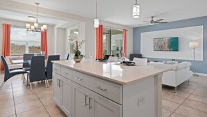 Een moderne keuken met een centraal eiland, een eethoek met stoelen, en een zithoek met een bank en televisie.