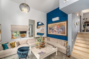 Ein Wohnzimmer mit einem Ecksofa, einem Couchtisch, einem blauen Sessel und einem großen Gemälde an der Wand.