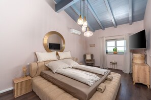 Ein Schlafzimmer mit einem großen Bett, einem Fernseher, einem runden Spiegel und einer Decke mit sichtbaren Balken.
