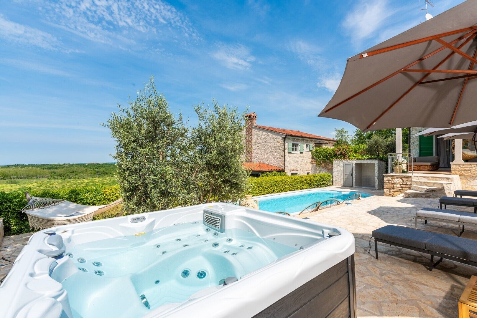 Un bain à remous, un espace salon extérieur, une piscine et un bâtiment en pierre avec un toit rouge.