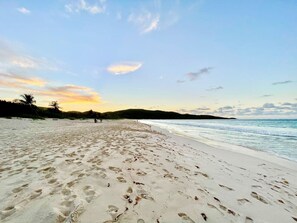 A beach with footprints, calm water, and a clear sky.