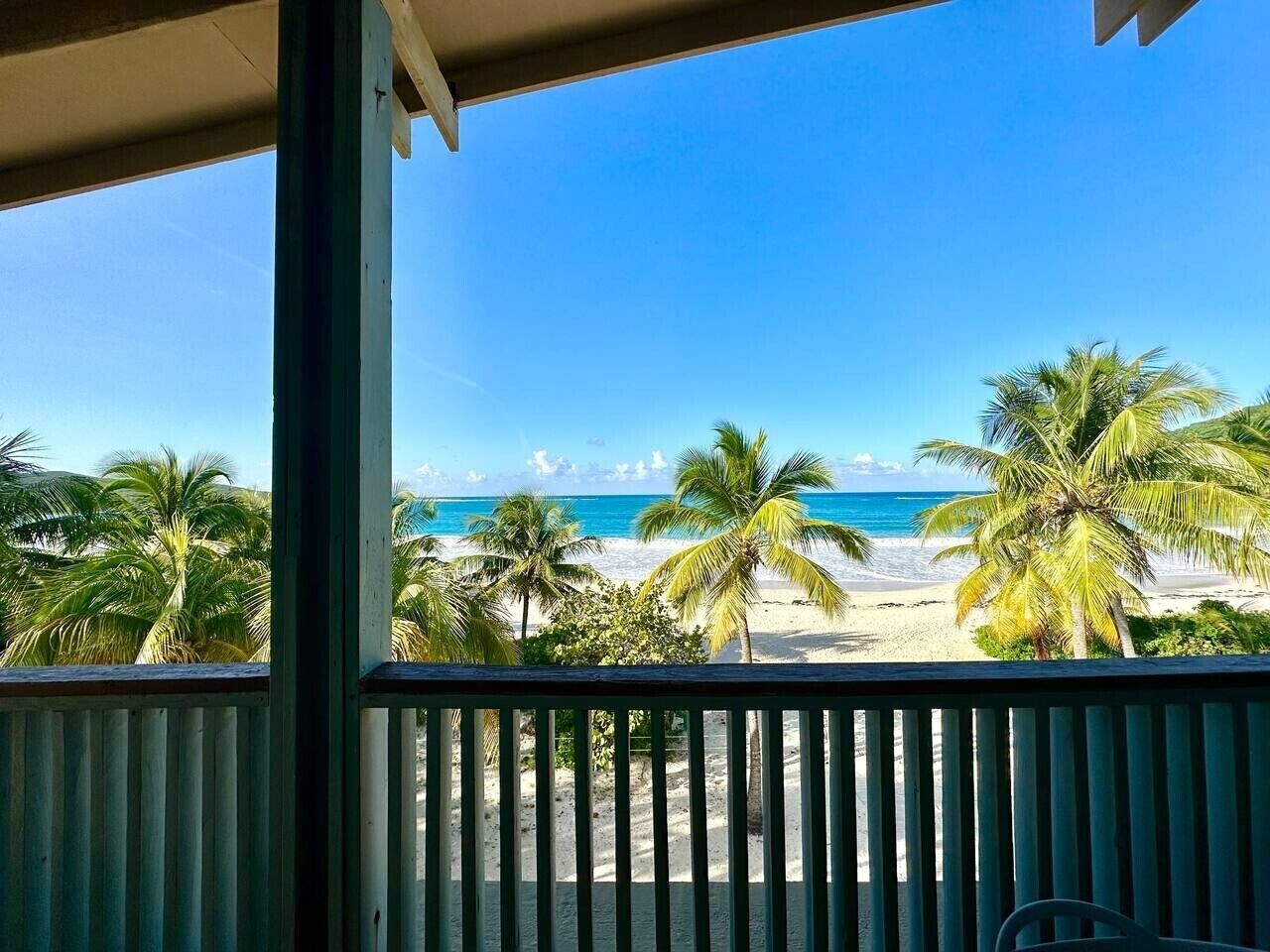 Une vue sur la plage depuis un balcon, avec des palmiers et un ciel dégagé.