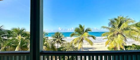 Une vue sur la plage depuis un balcon, avec des palmiers et un ciel dégagé.