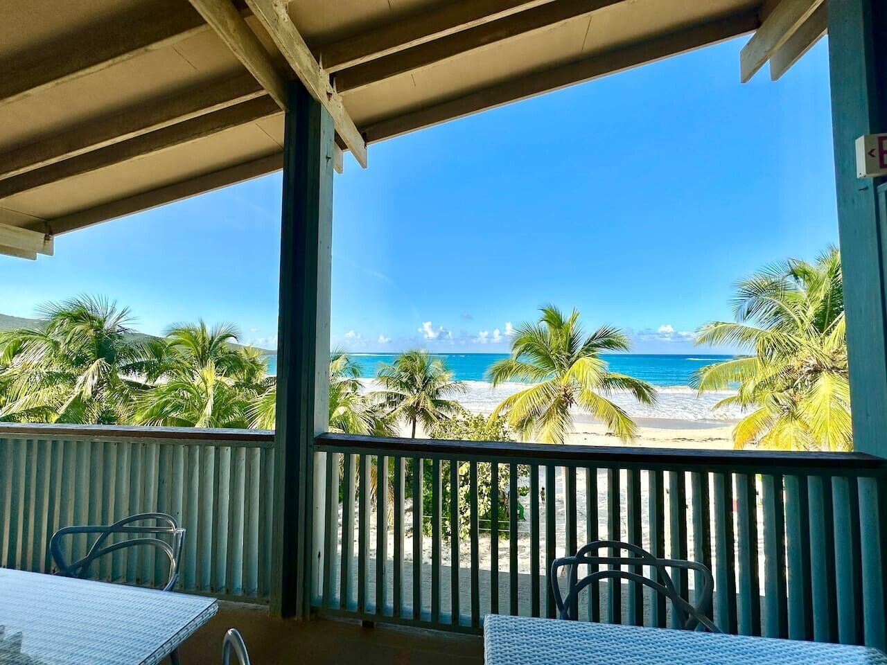 Un balcon avec vue sur une plage, des palmiers et un ciel dégagé.