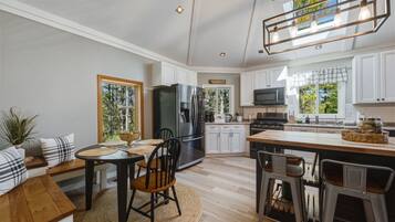 A modern kitchen with white cabinets, a stainless steel refrigerator, a microwave, and a dining area with a table and chairs.