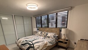 Een slaapkamer met een bed, nachtkastjes, een bureau en een raam met zonwering.