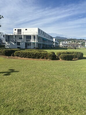 A multi-story building with balconies, a well-maintained lawn, and a clear sky. - Beach Front - Steps to beach 2-bdr remodeled Apt in Río Grande (Río Grande)