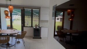 Een modern interieur met een eethoek, een kleine kitchenette en een groot raam met zonwering.