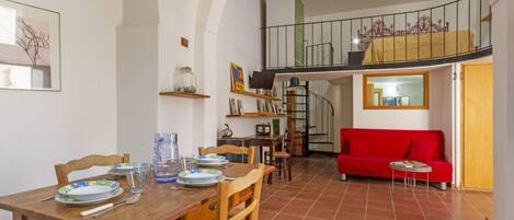 A dining area with a wooden table and chairs, a red sofa, and a staircase leading to an upper level.