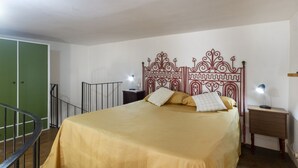 Een slaapkamer met een bed, een groene deur, een metalen leuning en een nachtkastje met een lamp.