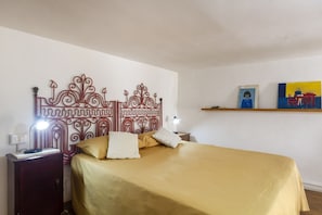 Un letto con testiera decorativa, una lampada da comodino, un comodino e una mensola con opere d'arte.