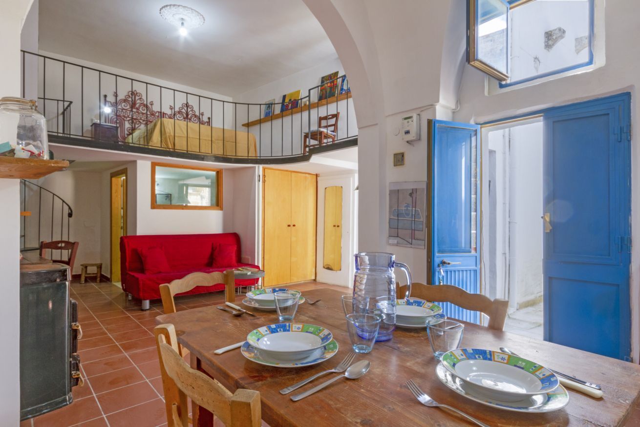 A dining area with a wooden table set for four, a red sofa, and a staircase leading to an upper level.