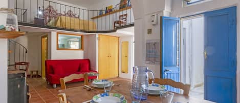 A dining area with a wooden table set for four, a red sofa, and a staircase leading to an upper level.