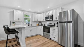 A modern kitchen with white cabinets, stainless steel appliances, and a wooden floor.