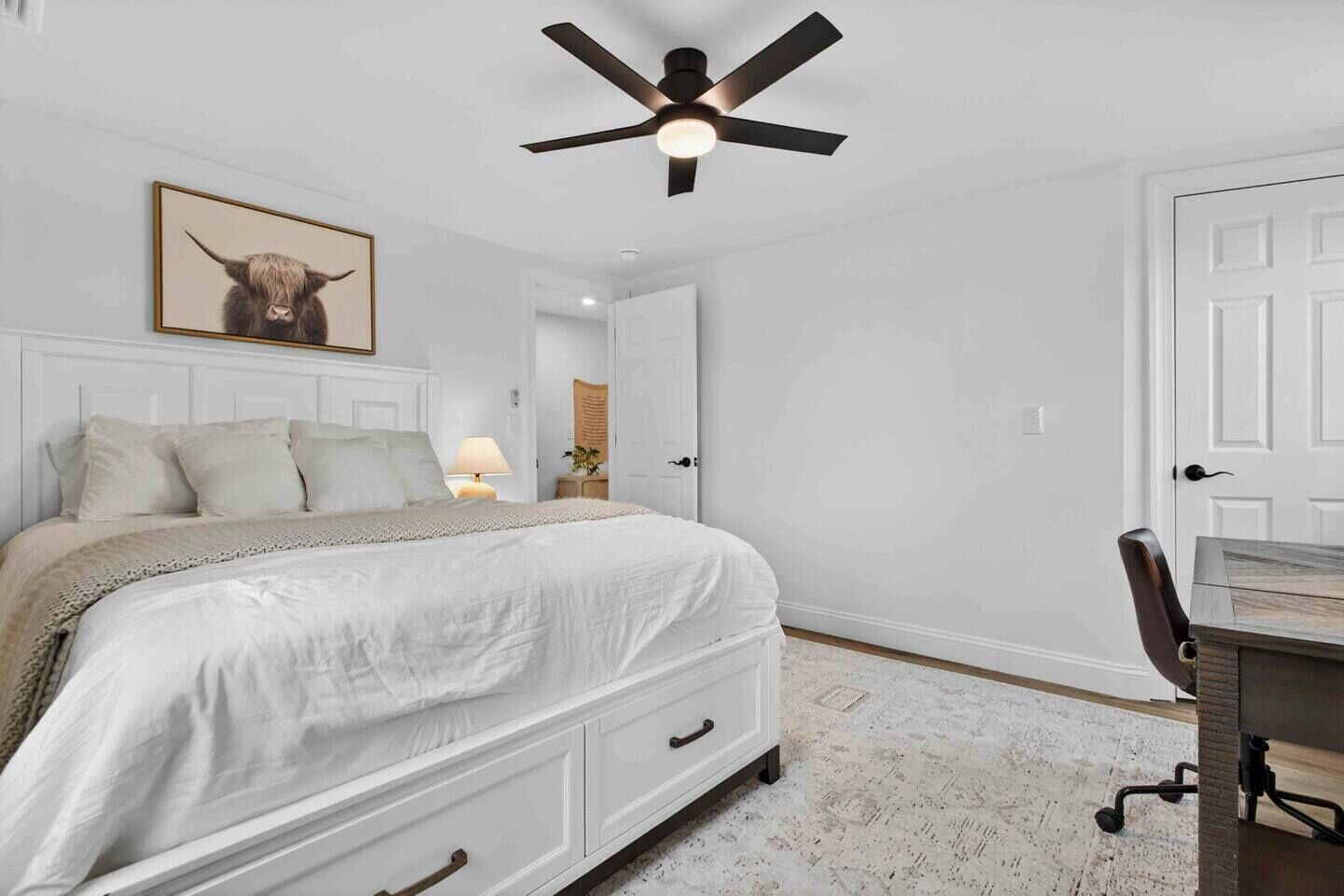 A bedroom with a bed, a desk, a ceiling fan, and a door.