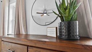 Une commode en bois avec des tiroirs, une plante en pot, une horloge murale et une citation encadrée.