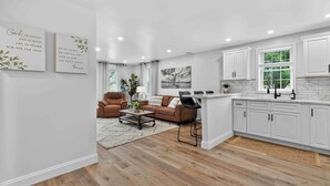 Une cuisine moderne aux meubles blancs, un coin repas avec un canapé en cuir marron et un salon avec une table basse et des fauteuils.