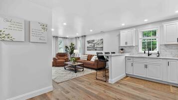 A modern kitchen with white cabinetry, a dining area with a brown leather couch, and a living room with a coffee table and chairs.
