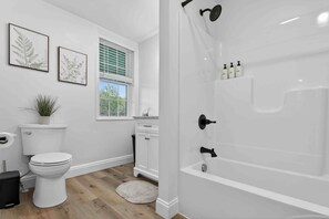 A bathroom with a toilet, sink, and bathtub, white walls, and a window with blinds. - Peaceful Country Escape & Animals (Ronks)