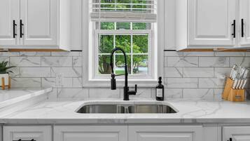 A kitchen with white cabinets, a marble countertop, a black faucet, and a window with blinds.