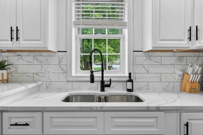 A kitchen with white cabinets, a marble countertop, a black faucet, and a window with blinds. - Peaceful Country Escape & Animals (Ronks)