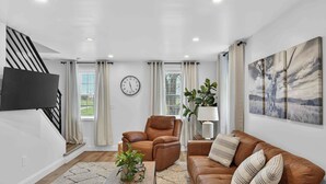 Un salon moderne comprenant un canapé, un fauteuil et une table basse, un téléviseur à écran plat fixé au mur et un escalier.