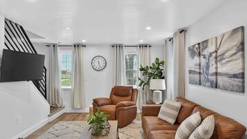 A modern living room with a sofa, armchair, and coffee table, a flat-screen TV mounted on the wall, and a staircase.