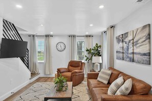 A modern living room with a sofa, armchair, and coffee table, a flat-screen TV mounted on the wall, and a staircase. - Peaceful Country Escape & Animals (Ronks)