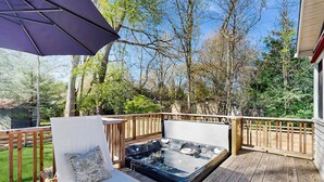Een hottub op een houten terras met een houten leuning en een lounge stoel met een kussen.
