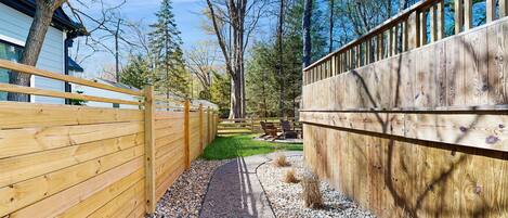 A wooden fence, gravel path, and a grassy area with trees and a building in the background.